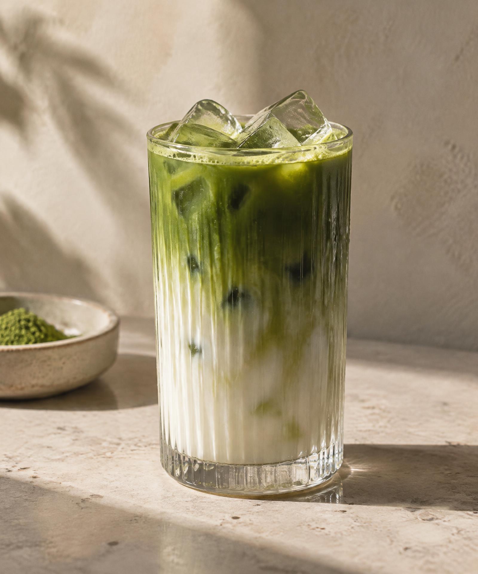 Iced matcha latte in a ribbed glass with ice, warm daylight and soft shadows